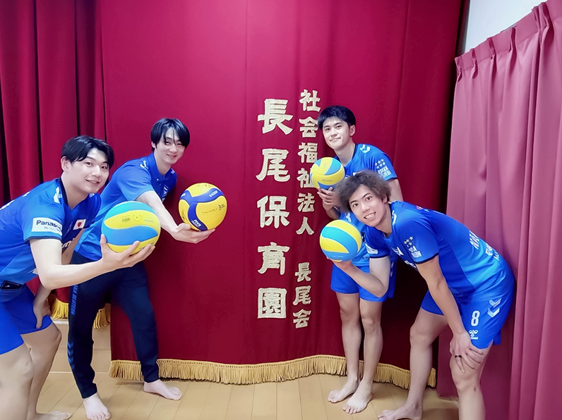 写真:学校名の前でポーズをとる竹内マネージャー、牧山マネージャー、中村選手、仲本選手