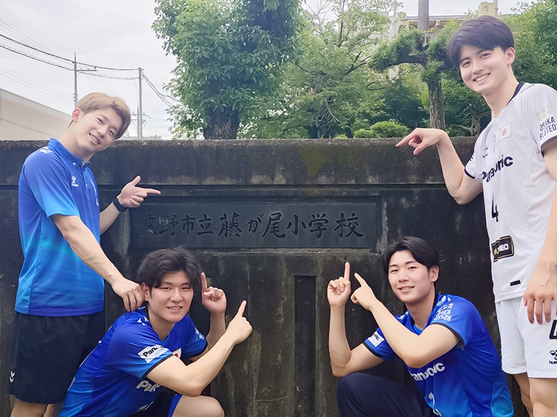 写真:学校名の前でポーズをとる山口コーチ、池城選手、竹内マネージャー、金田選手