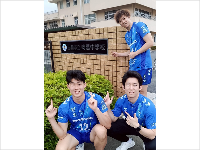 写真:会場名の前でポーズをとる野添選手、山口コーチ、仲本選手