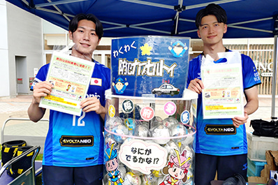写真：カプセルトイの容器をアピールする竹内マネージャーと金田選手