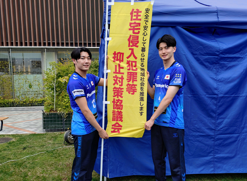画像:『住宅侵入犯罪等 抑止対策協議会』ののぼり旗をアピールする金田選手と竹内マネージャー