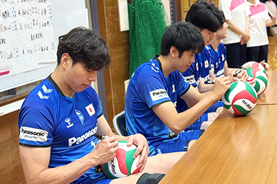 写真：ボールにサインをする選手とマネージャー（清水選手、中村選手、金田選手、竹内マネージャー）